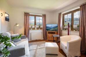 Ein Wohnzimmer mit einer Couch, einem weißen Sessel, einem Fernseher und einer Heizung.