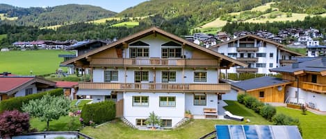 A multi-story building with a balcony, surrounded by a green landscape and hills.