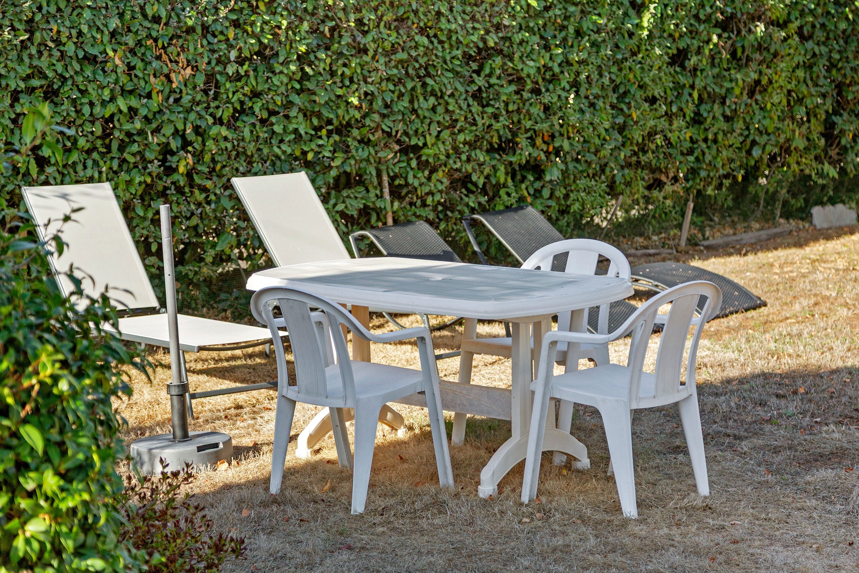 A round outdoor table with four chairs, surrounded by a hedge.