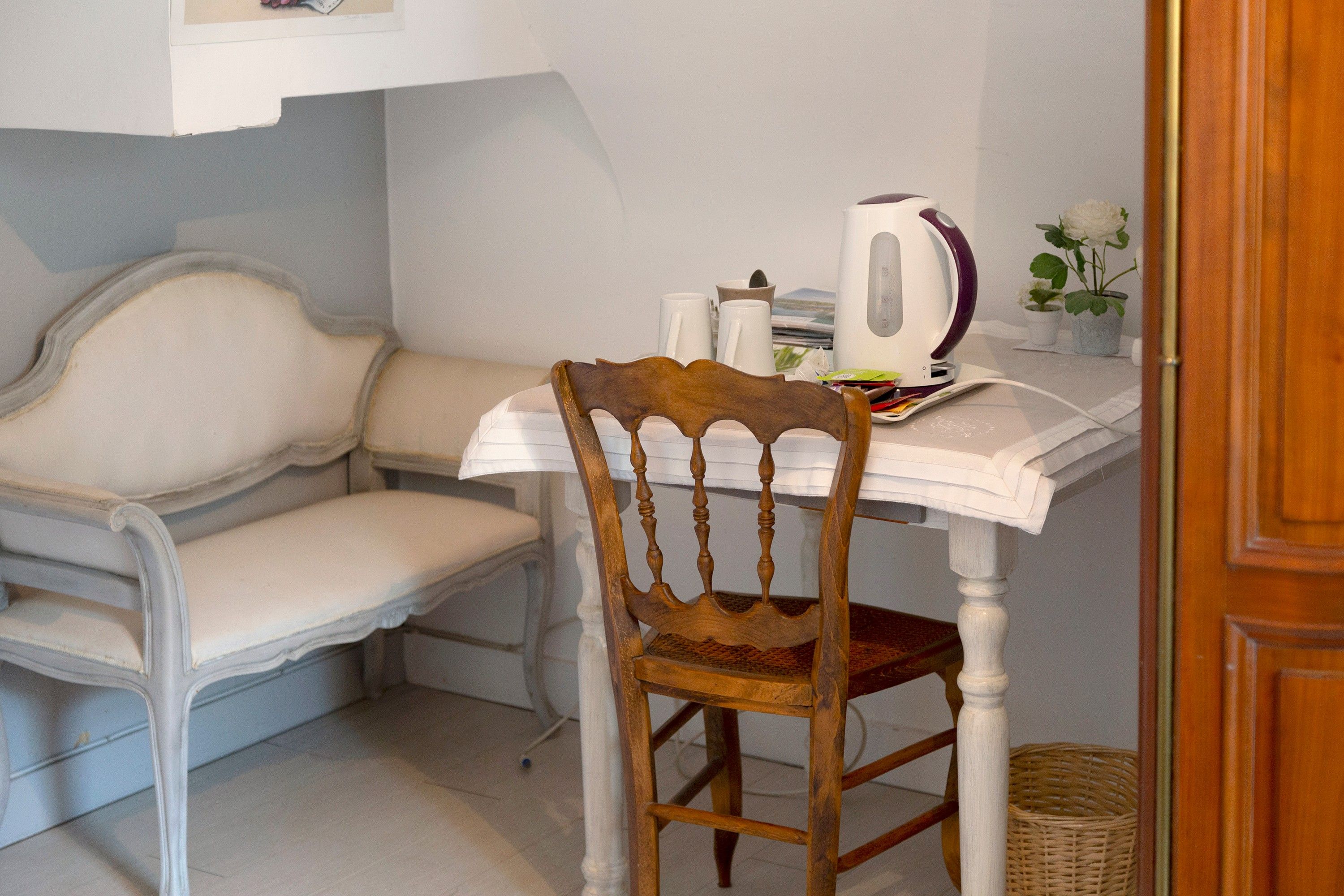 A small, cozy room with a wooden chair, a white table, and a kettle.