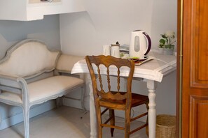 Una habitación pequeña y acogedora con una silla de madera, una mesa blanca y un hervidor.