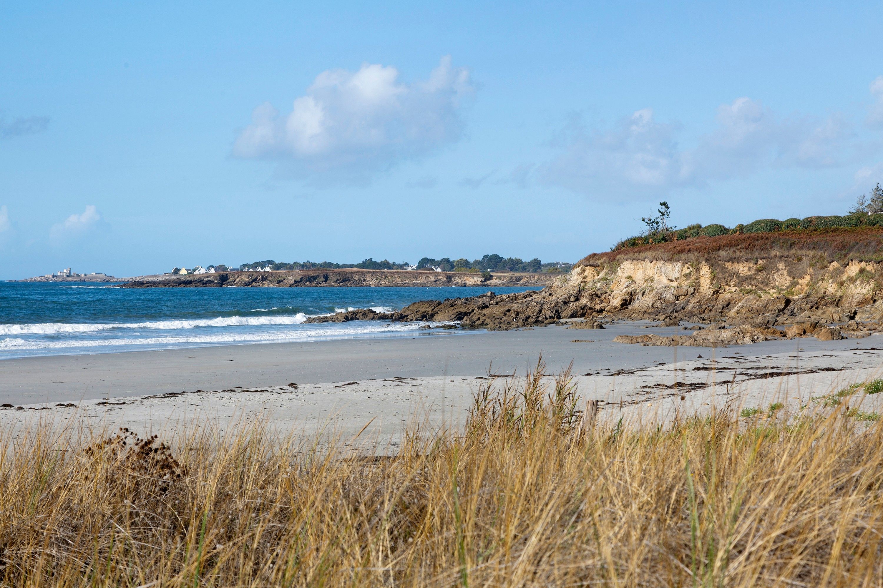 A coastal beach with rocky cliffs and a clear sky.