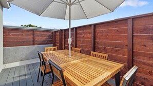 Eine Terrasse im Freien mit einem Holztisch, Stühlen, einem weißen Sonnenschirm und einem Holzzaun.