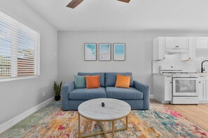 A modern living room with a sofa, a coffee table, and a kitchen area with white cabinets and appliances. - Vista Home Base | Parking, Near Beaches & Shops (Vista)