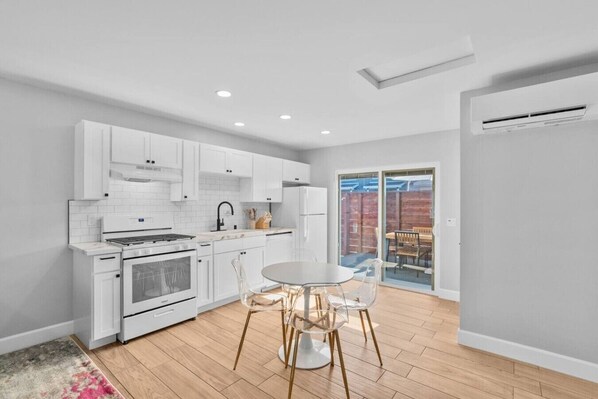 A modern kitchen with white cabinetry, a gas stove, and a dining area with a round table and chairs.