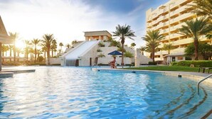 Una piscina con cascada, rodeada de palmeras y un edificio con balcones.