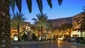 Un patio de hotel con palmeras, una piscina y un edificio de varios pisos con balcones.