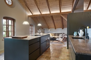 A modern kitchen with a large island, pendant lighting, and a view to a living area with a sofa and a chair. - The Krämerhaus by Alpine Host Helpers (Kirchberg in Tirol)