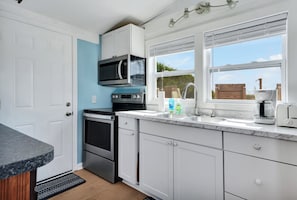 A modern kitchen with white cabinets, a built-in microwave, a stove, and a coffee maker. - Cozy ocean front 3-bedroom cottage in beautiful Carolina Beach (Carolina Beach)
