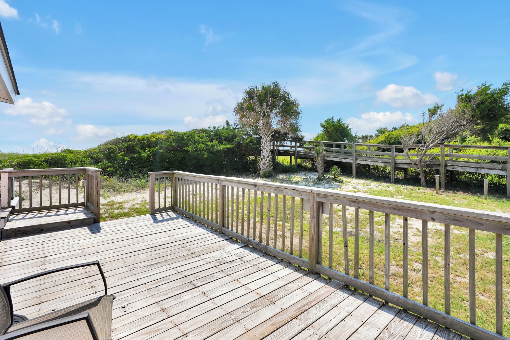 A wooden deck with a railing overlooking a beach and a wooden bridge.