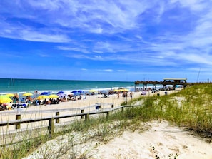 Une plage avec une promenade en bois, des parasols et des gens qui profitent de la mer.