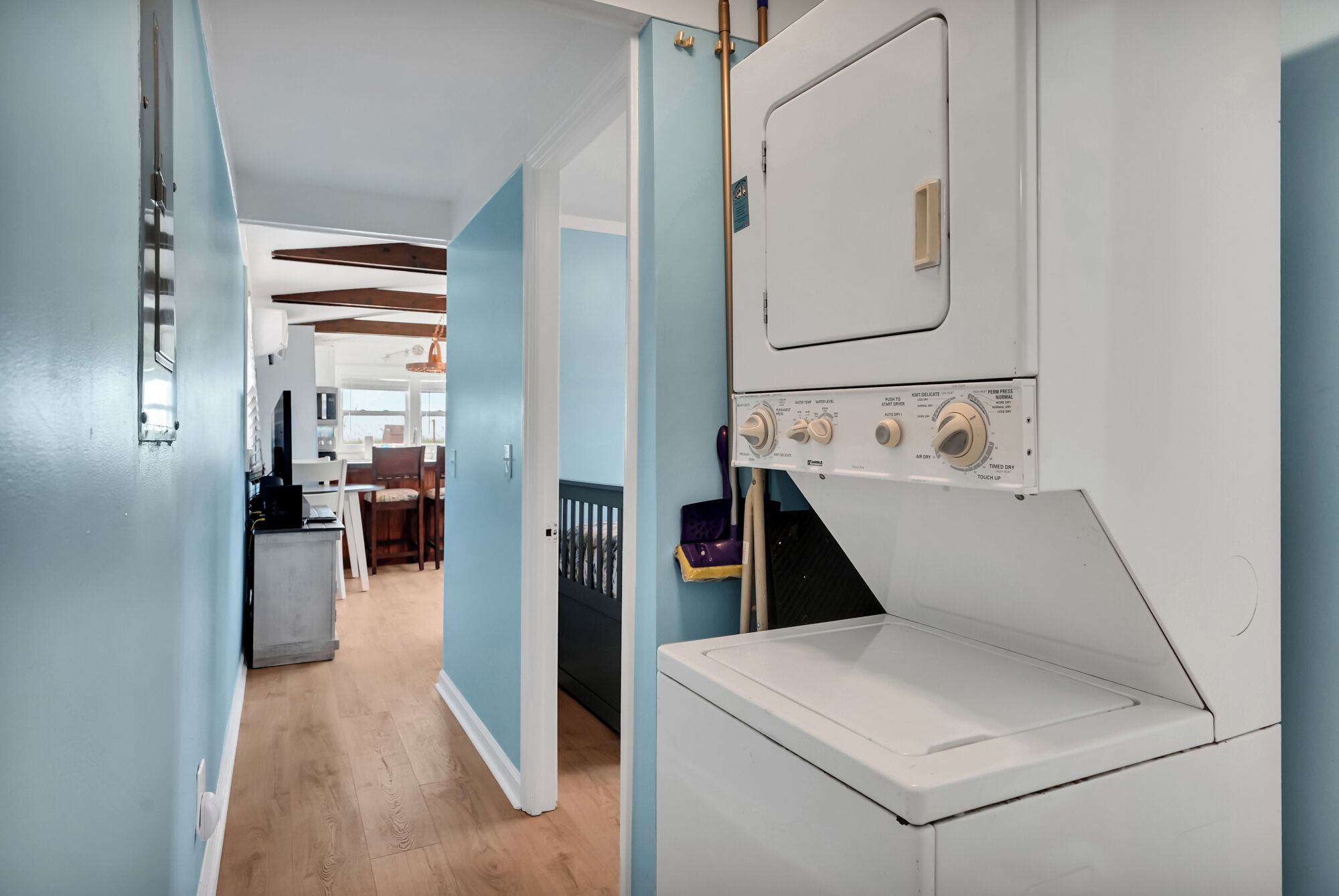Lavandería con lavadora y secadora, suelo de madera y vista hacia un comedor.