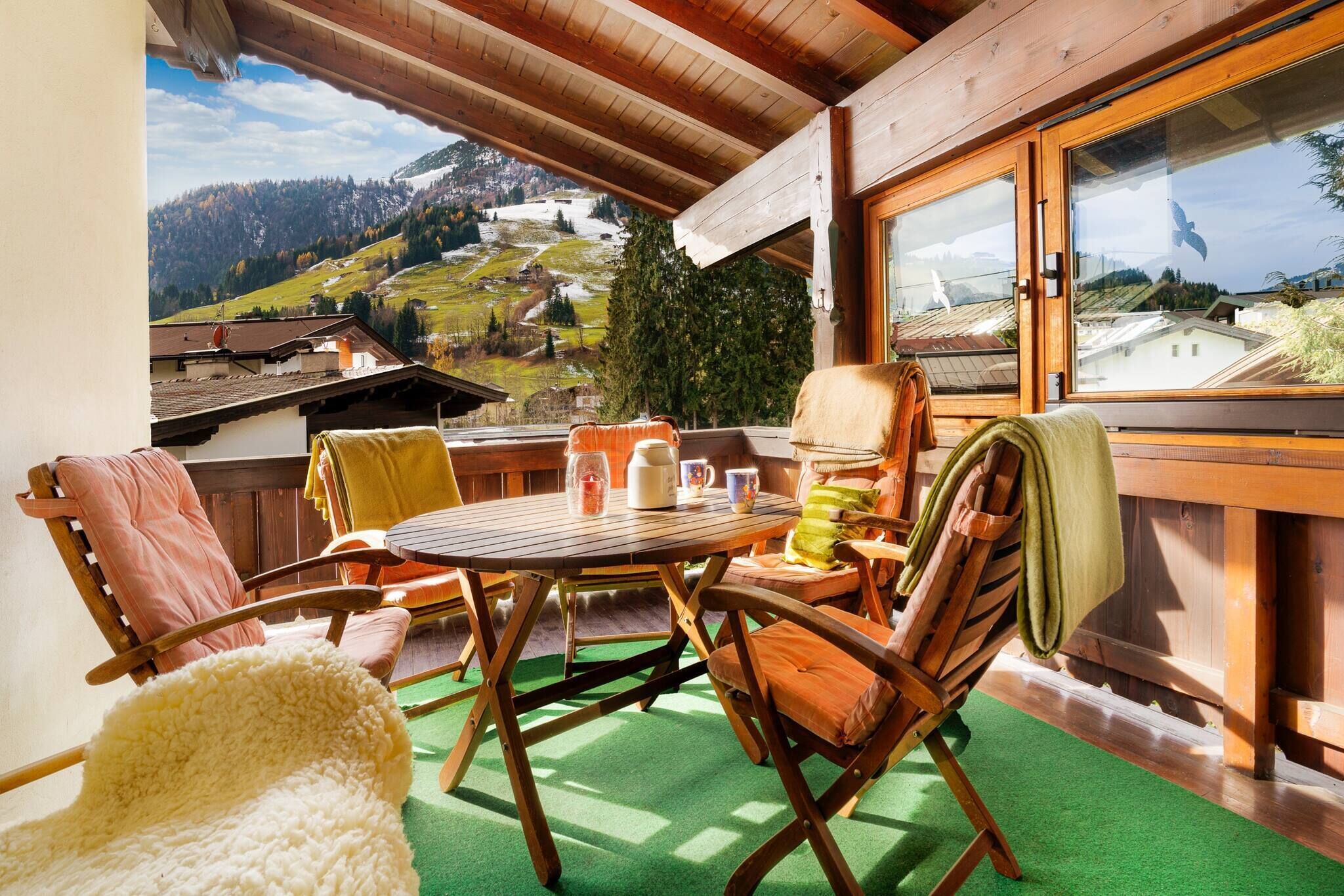 A wooden deck with a table and chairs, a view of a mountainous landscape, and a window with a view of a bird.