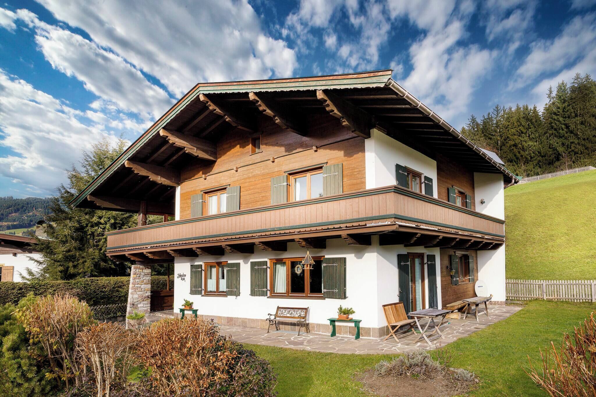 A two-story chalet with a balcony, stone foundation, and a view of the surrounding landscape.
