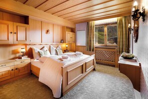 Ein Schlafzimmer aus Holz mit einem großen Bett, Einbauschränken, einem Fenster mit Vorhängen und einem kleinen Tisch mit einer Lampe.