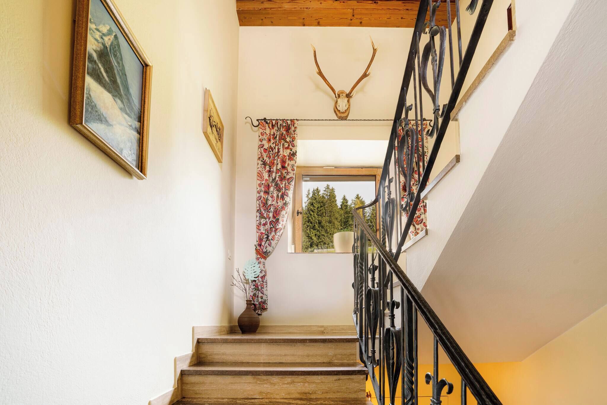 A wooden staircase with a black metal railing, a deer skull decoration, and a window with a view of trees.