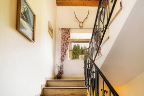Eine Holztreppe mit schwarzer Metallreling, einer Dekoration mit einem Hirschschädel und einem Fenster mit Blick auf Bäume.