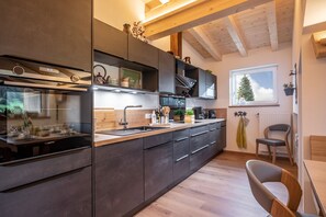A modern kitchen with dark cabinetry, a stainless steel range hood, and a window with a view of a tree. - Maria's Alpine Apartment (Brixen im Thale)
