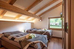 Ein Schlafzimmer mit zwei Betten, Holzbalken, einem großen Fenster und Blick auf ein Gebäude.