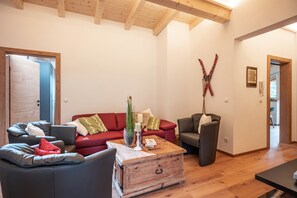 A cozy living room with a red sofa, a grey armchair, and a wooden coffee table. - Maria's Alpine Apartment (Brixen im Thale)