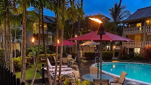 A poolside area with lounge chairs, umbrellas, and a pool. - Kailua Kona Islander | Steps to Beach, Lanai, Pool (Kailua-Kona)