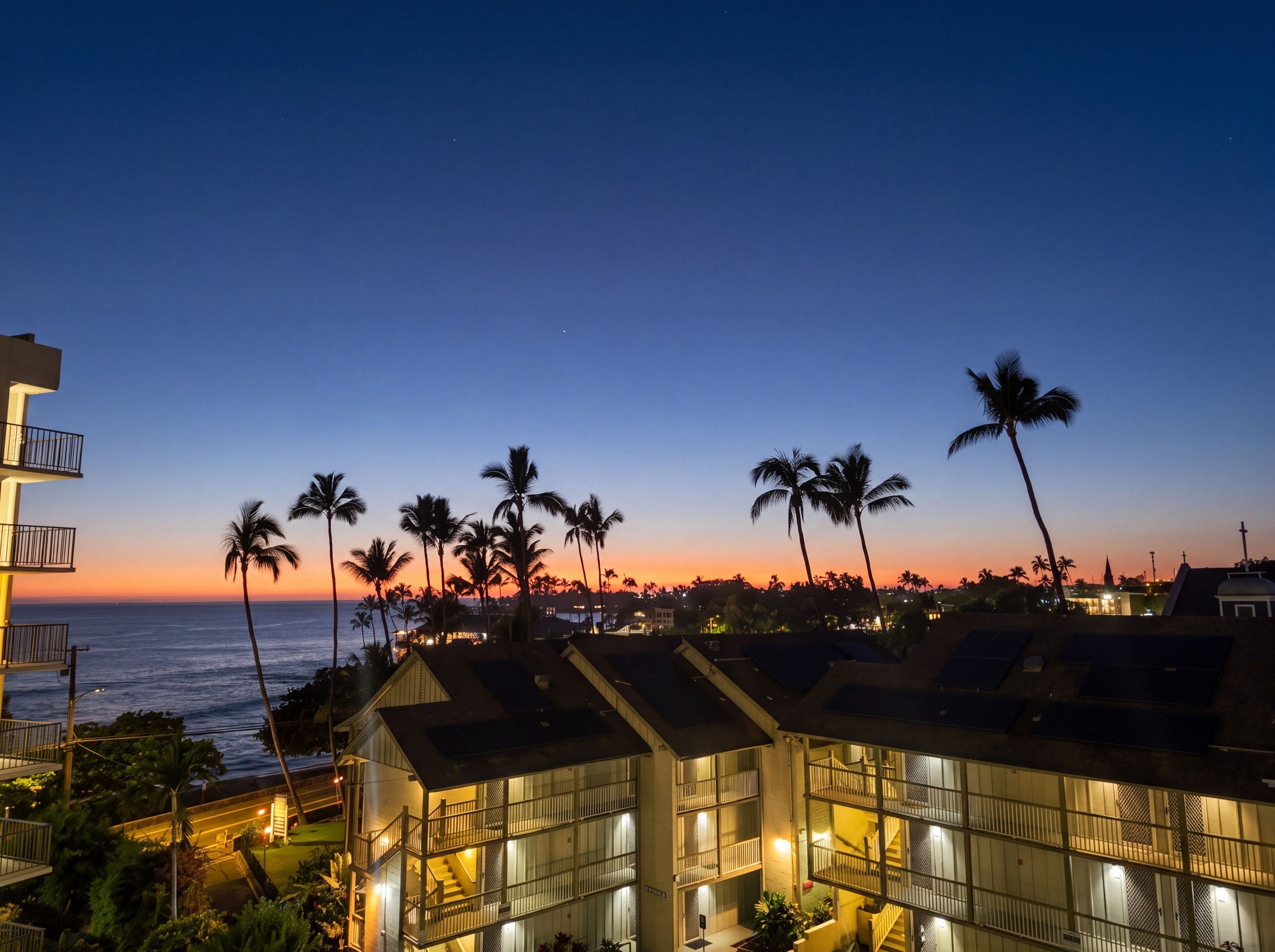 A coastal hotel with multiple floors, balconies, and a view of the ocean at sunset.