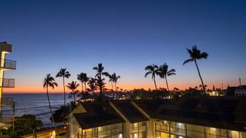 A coastal hotel with multiple floors, balconies, and a view of the ocean at sunset.