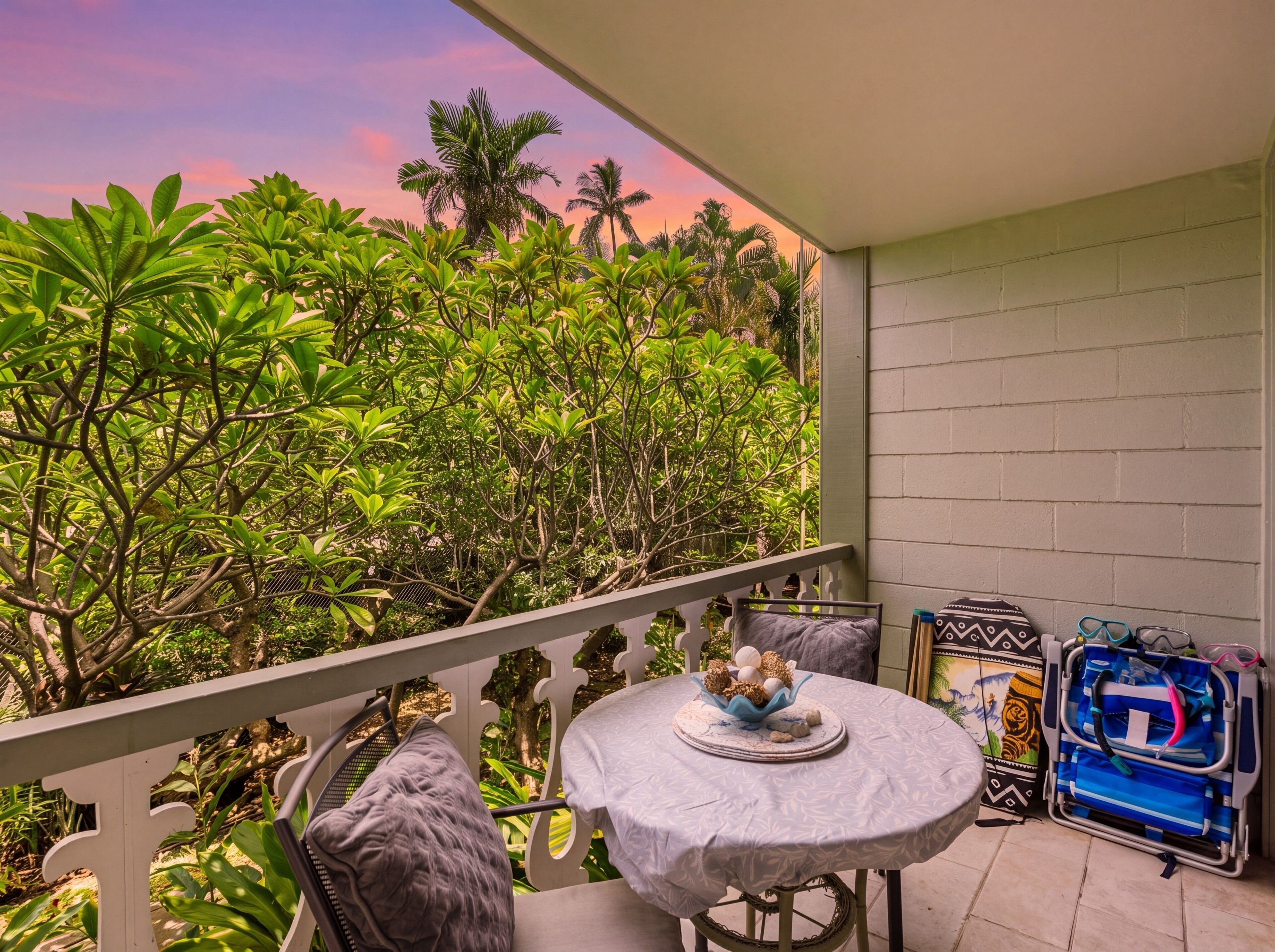 A balcony with a round table, chairs, and a view of dense greenery.
