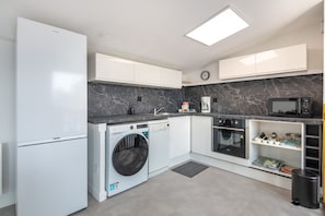A modern kitchen with white cabinetry, a built-in washing machine, a microwave, and an oven. - Le massif de Belledonne - Duplex avec terrasse (Meylan)