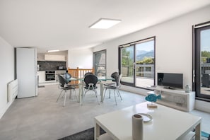 A modern living room with a dining area, a kitchen, and a balcony with a mountain view. - Le massif de Belledonne - Duplex avec terrasse (Meylan)