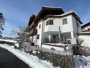A multi-story building with a white facade, wooden balconies, and a snow-covered ground. - KitzAlps Standard Apartment (Kirchberg in Tirol)
