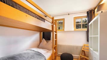 A compact room with bunk beds, a radiator, a window with curtains, and a wardrobe.