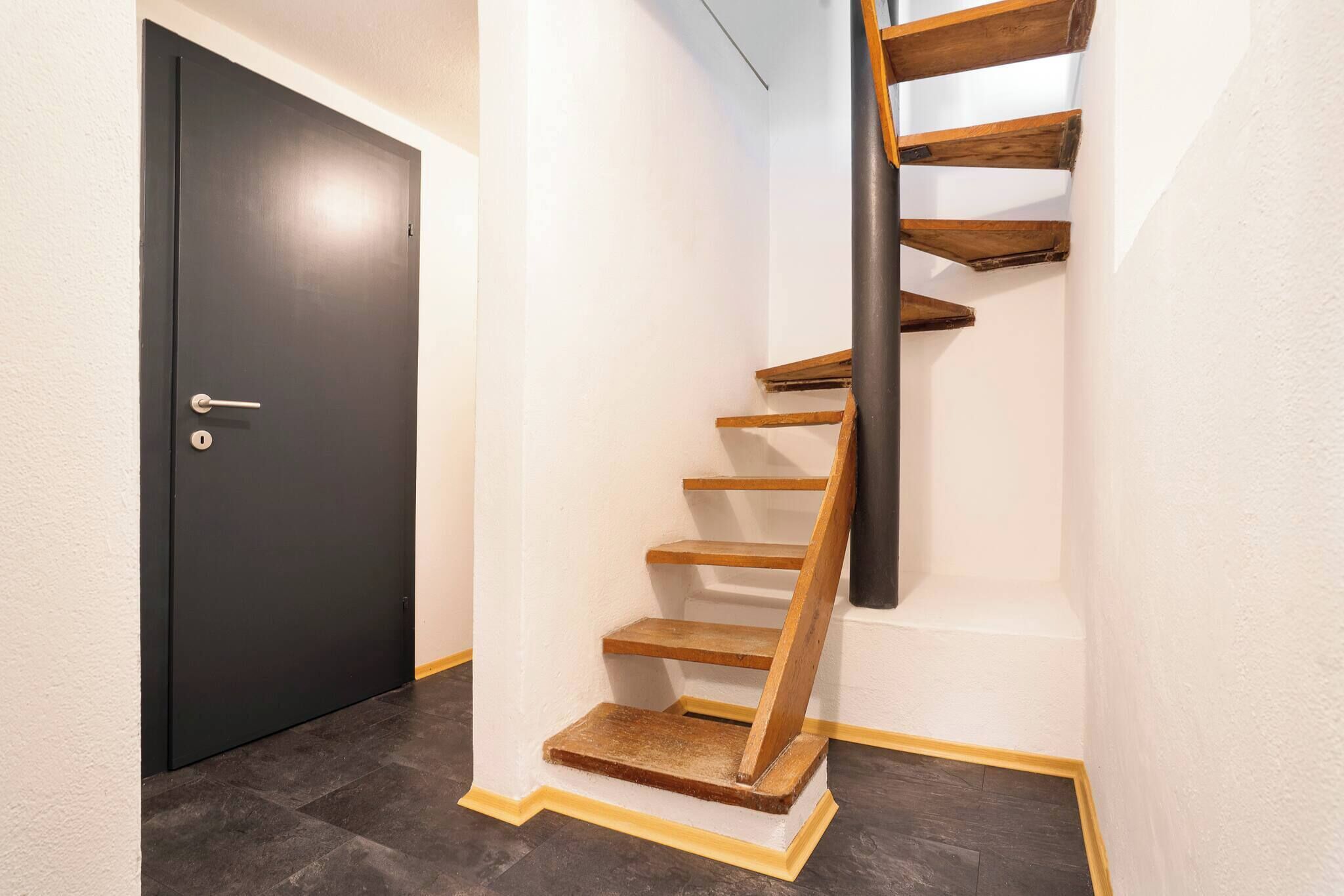 A staircase with wooden steps and a black handrail, leading to a dark door.