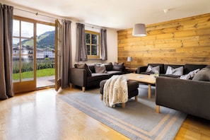 A modern living room with a sofa set, a coffee table, and a view of a mountainous landscape through large windows. - KitzAlps Standard Apartment (Kirchberg in Tirol)