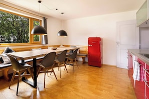 A modern kitchen with a wooden dining table, chairs, a red refrigerator, and a window with a view of trees. - KitzAlps Standard Apartment (Kirchberg in Tirol)