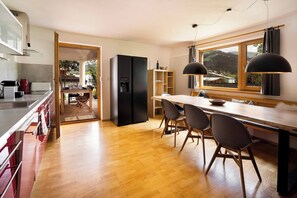 A modern kitchen with a wooden dining table and chairs, a black refrigerator, and a view through the window. - KitzAlps Apartment Top 1 (Kirchberg in Tirol)