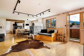 A spacious living area with a wooden floor, a sofa, a dining table, and a kitchen in the background. - KitzAlps Apartment Top 2 (Kirchberg in Tirol)