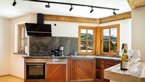 A kitchen with wooden cabinets, a built-in oven, a coffee maker, and a view of the countryside through large windows. - KitzAlps Premium Apartment (Kirchberg in Tirol)
