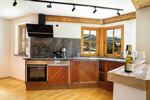 A kitchen with wooden cabinets, a built-in oven, a coffee maker, and a view of the countryside through large windows. - KitzAlps Premium Apartment (Kirchberg in Tirol)