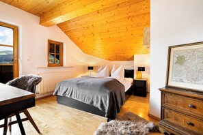 Une chambre avec un plafond en pente, un lit avec des oreillers, une table de chevet, une carte accrochée au mur et une vue par la fenêtre.