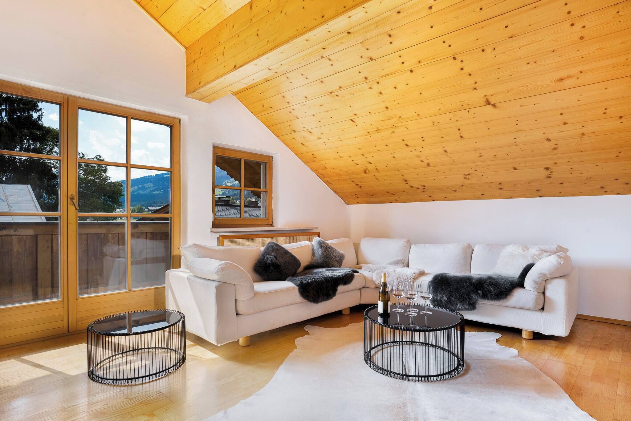 A spacious loft with a high ceiling, a white sofa set, two round black tables, and large windows offering a view of the outdoors.