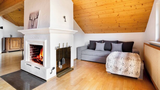 A cozy living room with a fireplace, a grey sofa, and a wooden ceiling. - KitzAlps Premium Apartment (Kirchberg in Tirol)