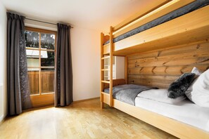 A bunk bed with a wooden headboard, a sofa with a cushion, and a window with curtains. - KitzAlps Apartment Top 2 (Kirchberg in Tirol)