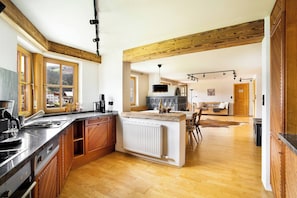 Une cuisine moderne dotée d’un îlot central, de poutres en bois et offrant une vue sur un paysage montagneux grâce à de grandes fenêtres.