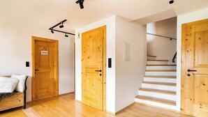 A wooden interior with a staircase, a bed with a white blanket, and a dog. - KitzAlps Premium Apartment (Kirchberg in Tirol)