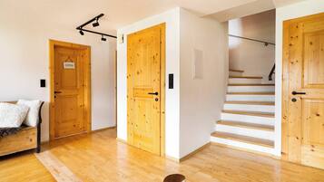 A wooden interior with a staircase, a bed with a white blanket, and a dog.