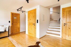A wooden interior with a staircase, a bed with a white blanket, and a dog. - KitzAlps Premium Apartment (Kirchberg in Tirol)