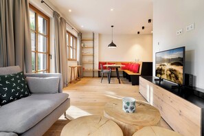 A modern living room with a sofa, a dining table, and a TV. - Garden Suite by Alpine Host Helpers (Kirchberg in Tirol)