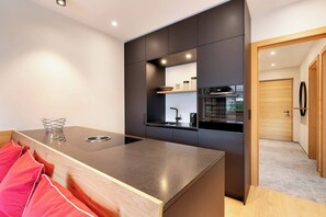 A modern kitchen with a central island, built-in appliances, and a wooden door leading to another room. - Garden Suite by Alpine Host Helpers (Kirchberg in Tirol)