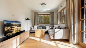Ein modernes Wohnzimmer mit großem Flachbildfernseher, einer Sofagarnitur, einem Couchtisch und einer Stehlampe.
